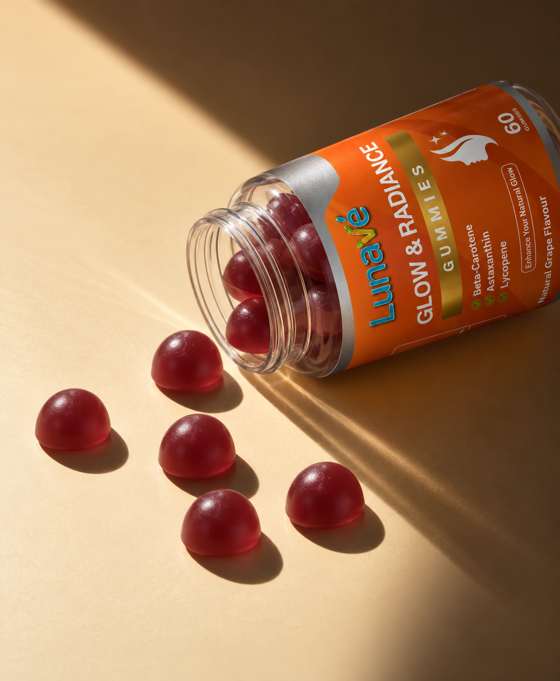 Lunavé Glow & Radiance tanning gummies spilled from bottle on warm golden surface - round dark red grape flavour gummies with Beta-Carotene, Astaxanthin and Lycopene.